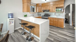 A modern kitchen with wooden cabinets, a large island with bar stools, a built-in microwave, and a water dispenser.