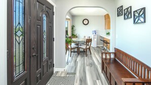 A hallway with a wooden bench, a dining area with a table and chairs, and a kitchen visible through an archway.