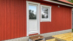 Een rood houten gebouw met twee ramen en een houten bankje ervoor.