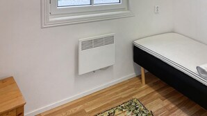 Een kamer met een raam, een witte radiator, een houten vloer en een bed met een witte matras.