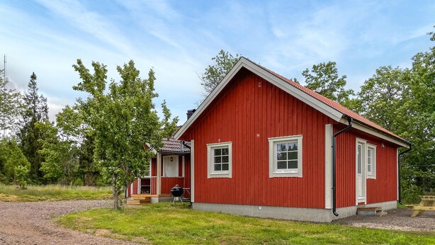 Een rode houten woning met schuin dak, een veranda en een klein terras.