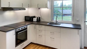 Een keuken met witte kasten, een magnetron, een broodrooster en een raam met uitzicht op groen.