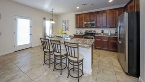 A modern kitchen with a central island, bar stools, a refrigerator, and wooden cabinets. - Amazing 4 Bedroom 3 Bathroom Complete House (Tucson)