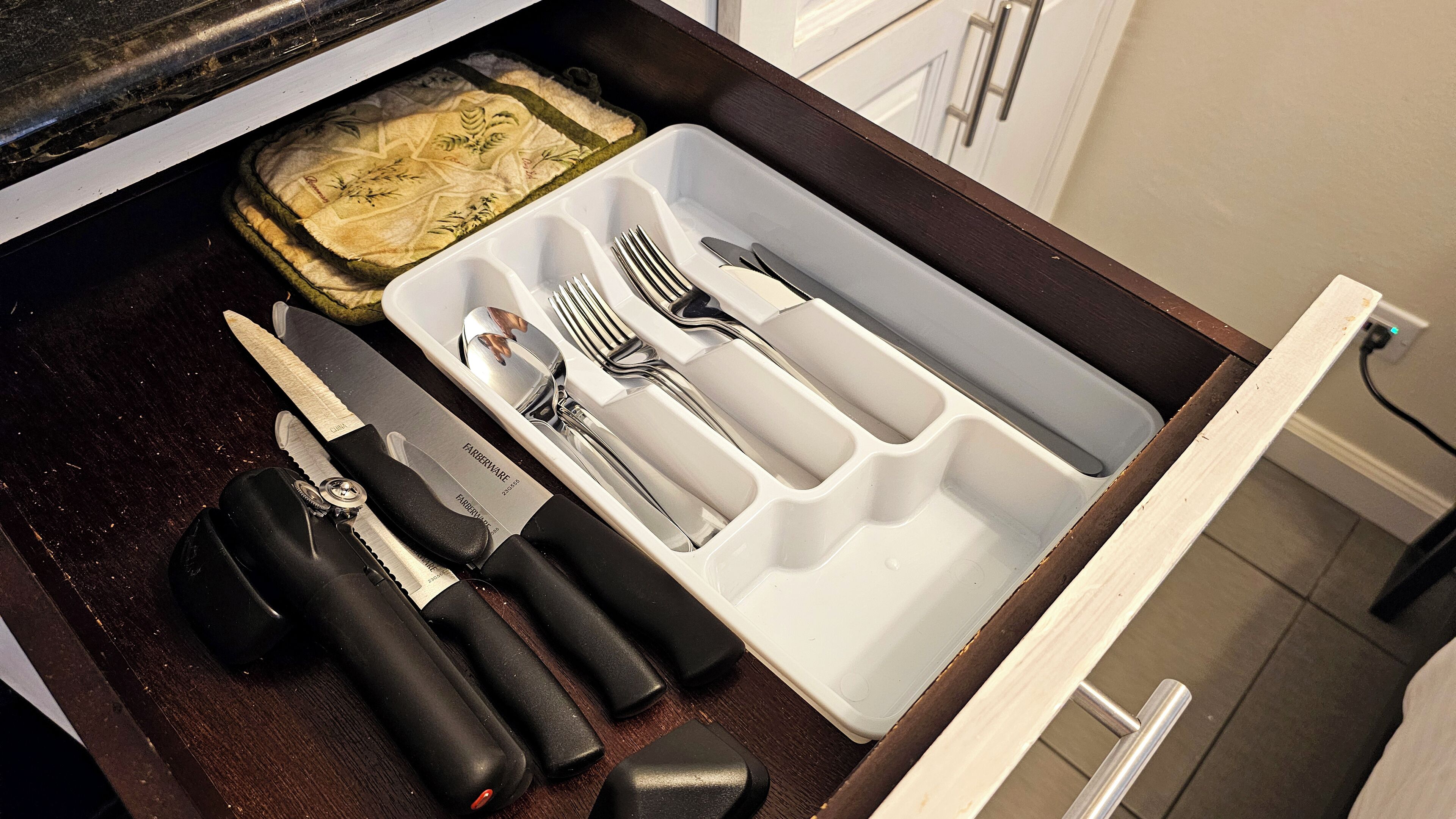 Un cajón de cocina con utensilios y tabla de cortar.