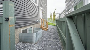 A narrow pathway leading to a house with a small wooden staircase and a metal bench.