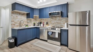 A modern kitchen with blue cabinets, a stainless steel refrigerator, a microwave, a dishwasher, and an oven.