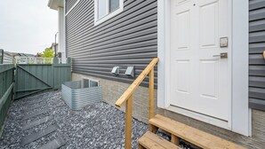 A residential building with a grey exterior, a white door, and a small outdoor seating area with a bench and a table.