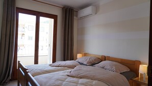 Une chambre d’hôtel avec deux lits, une tête de lit en bois, une table de chevet avec une lampe, un appareil de climatisation et une vue sur le balcon extérieur.