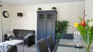 Un salon moderne avec un canapé, une table à manger et des chaises. On y trouve un meuble avec des portes en verre et une horloge au mur.