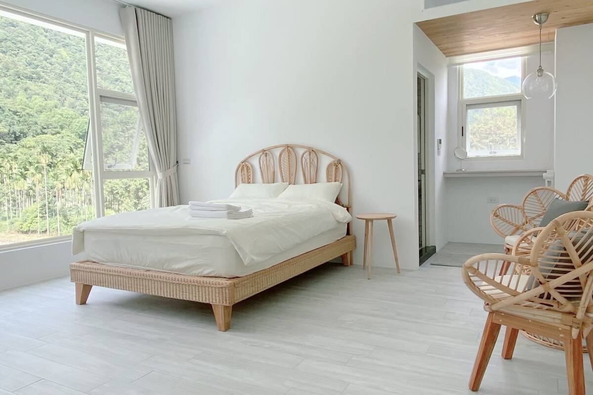 A bedroom with a large bed, a small bedside table, and wicker chairs.