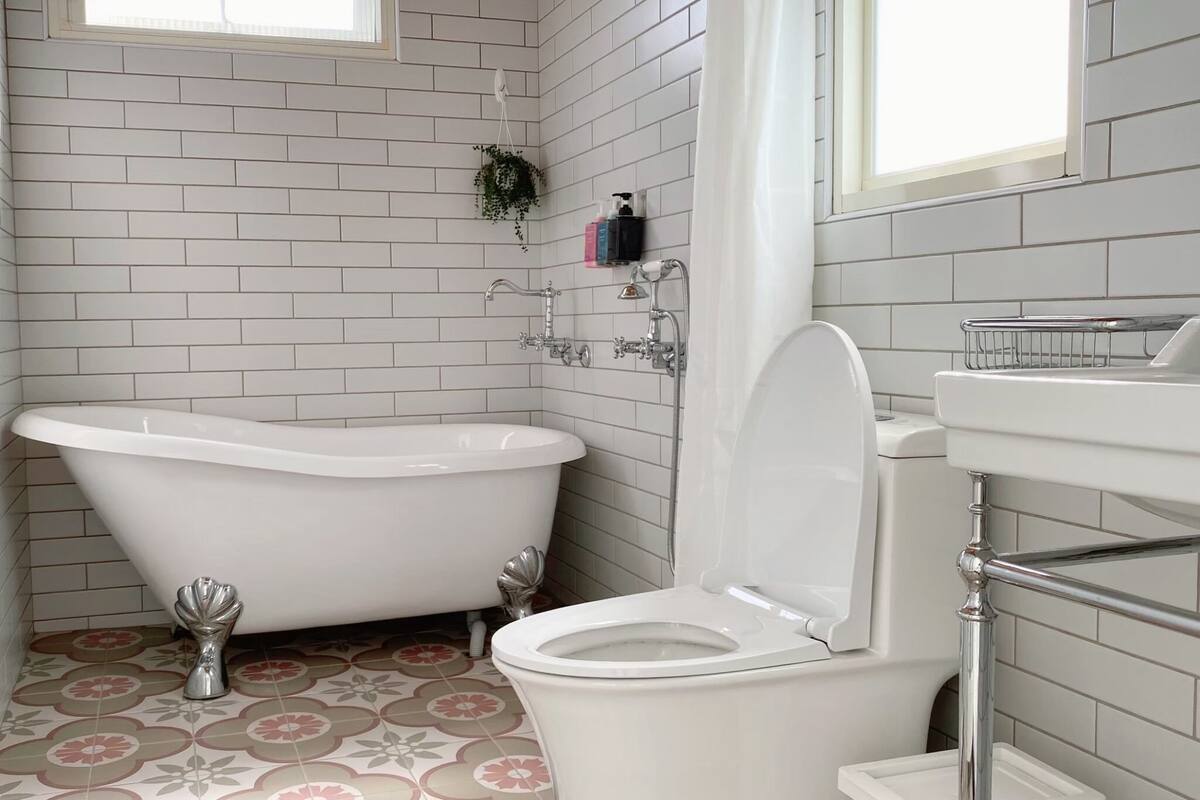 A bathroom with a white bathtub, a white toilet, and a tiled floor with a floral pattern.