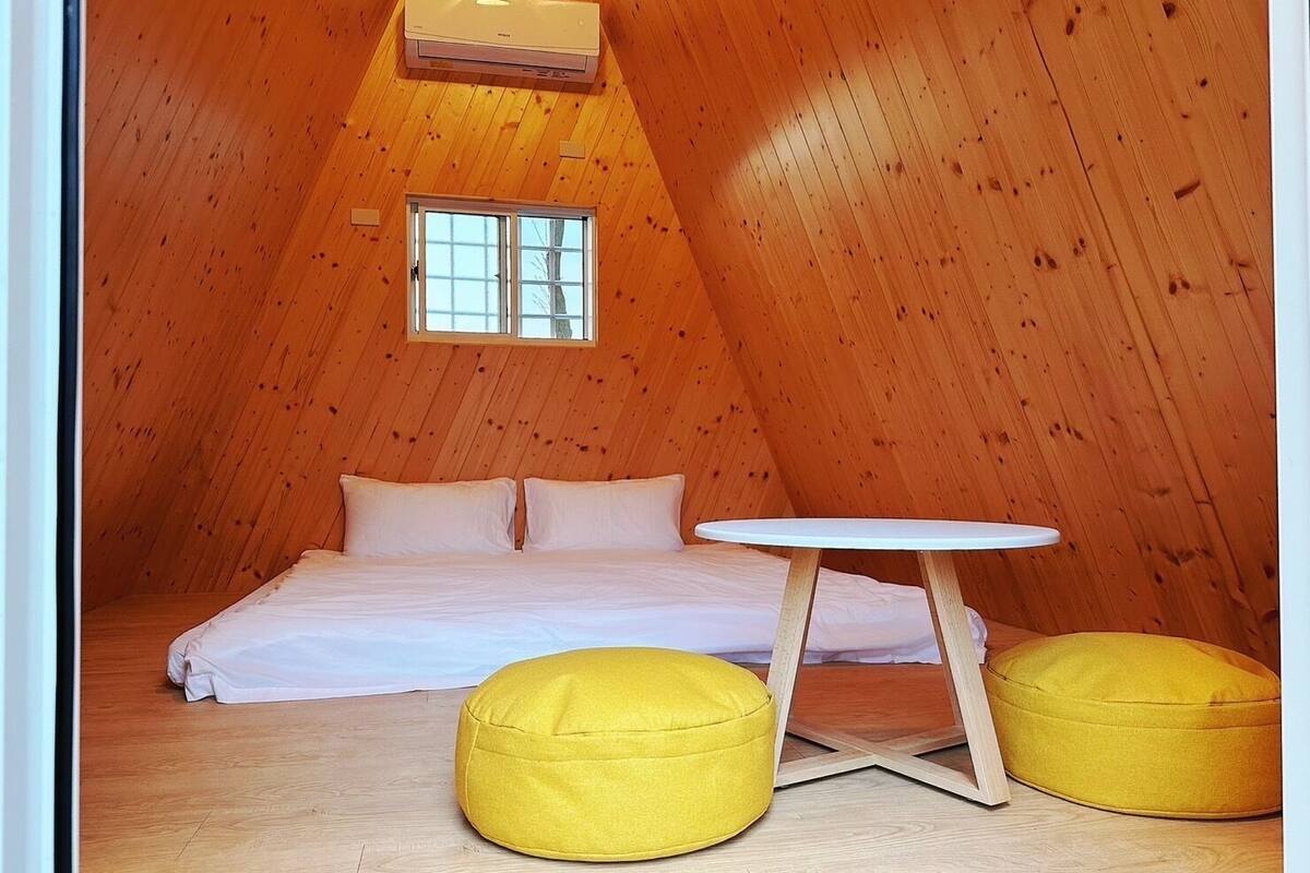 A cozy attic bedroom with a wooden sloped ceiling, a bed with white bedding, a small round table, and two yellow bean bag chairs.