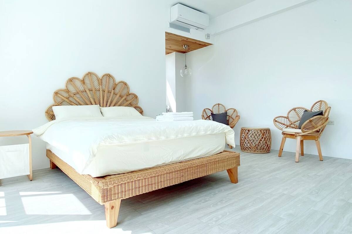 A modern bedroom with a large bed, wicker furniture, and a ceiling-mounted air conditioner.