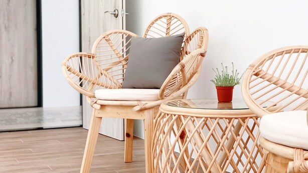 A wicker chair with a cushion and a small table with a potted plant. - guantau (Puli)