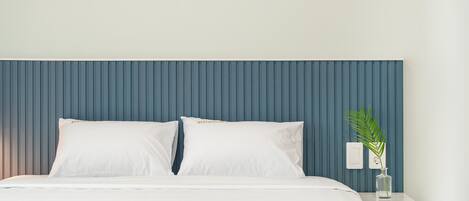 A bed with white bedding and two pillows, a blue headboard, and a bedside table with a clear vase containing a plant.