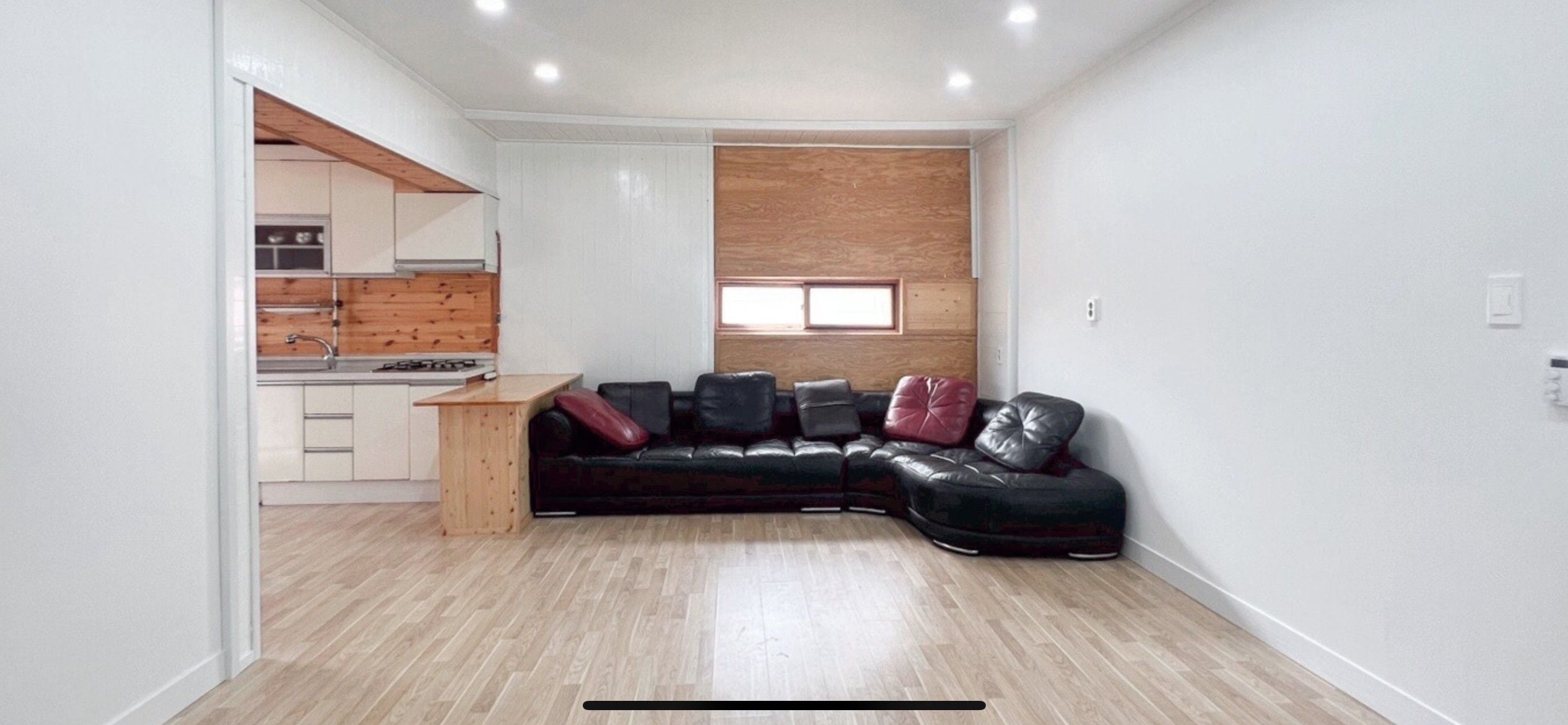 Un espacio habitable compacto con kitchenette, un sofá de cuero negro y una pared decorativa de madera.