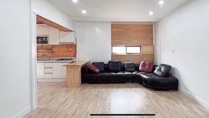A compact living space with a kitchenette, a black leather sofa, and a wooden accent wall. - Taean Yeonpo Haibada Pension (Taean)