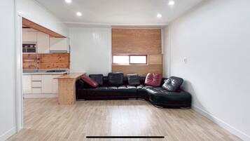 Un espacio habitable compacto con kitchenette, un sofá de cuero negro y una pared decorativa de madera.