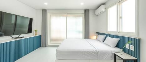 A modern bedroom with a bed, a TV mounted on the wall, and a window with curtains.