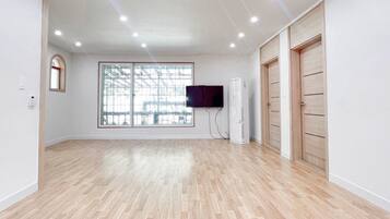 A room with a large window, a flat-screen TV mounted on the wall, and a wooden wardrobe.