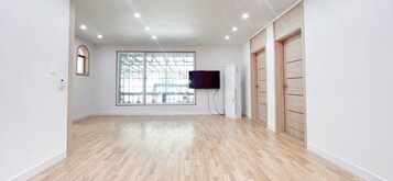 Una habitación con un ventanal grande, un televisor de pantalla plana en la pared y un armario de madera.