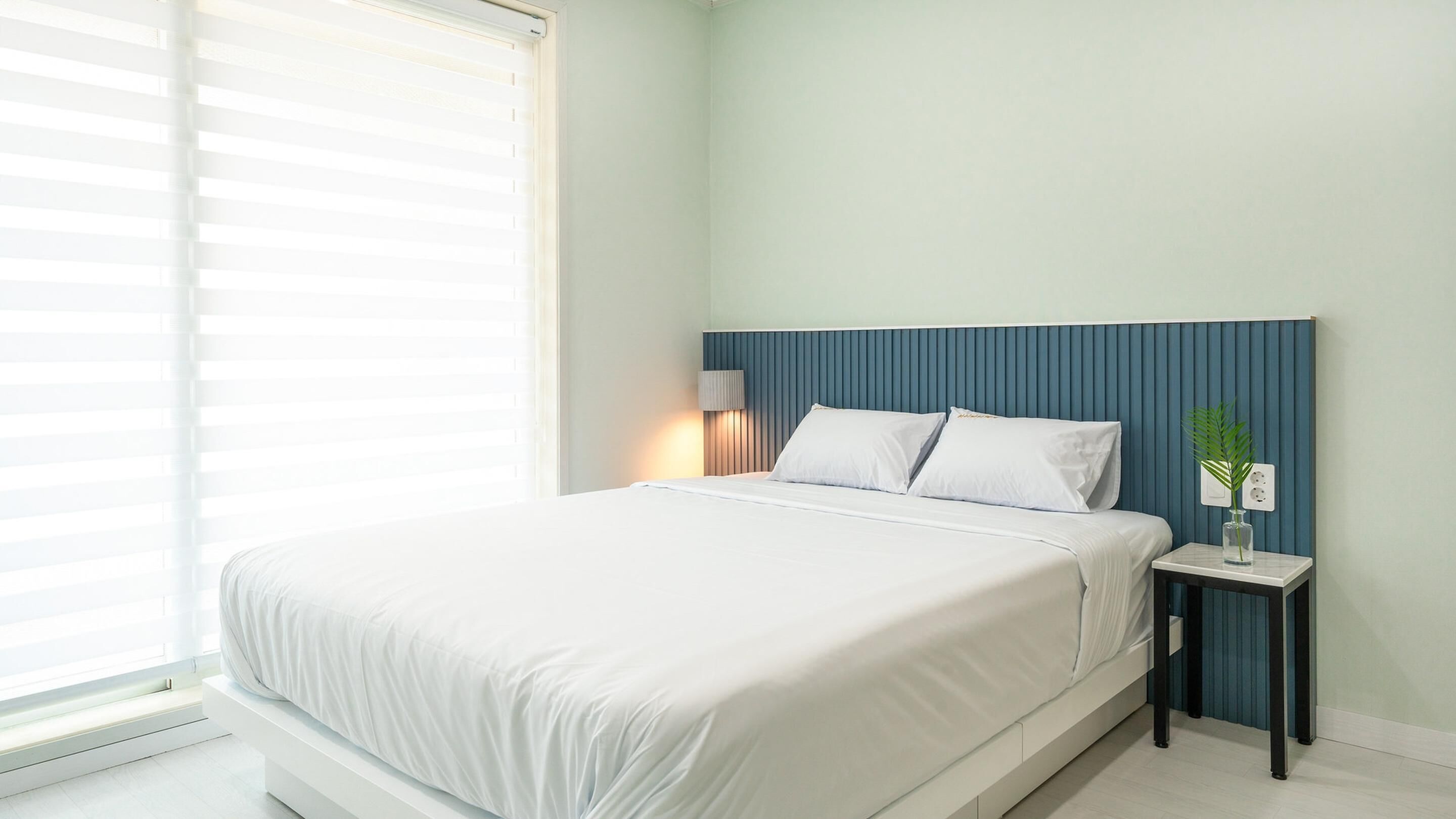 Ein modernes Schlafzimmer mit Bett, Nachttisch, Lampe und einem Blumentopf.