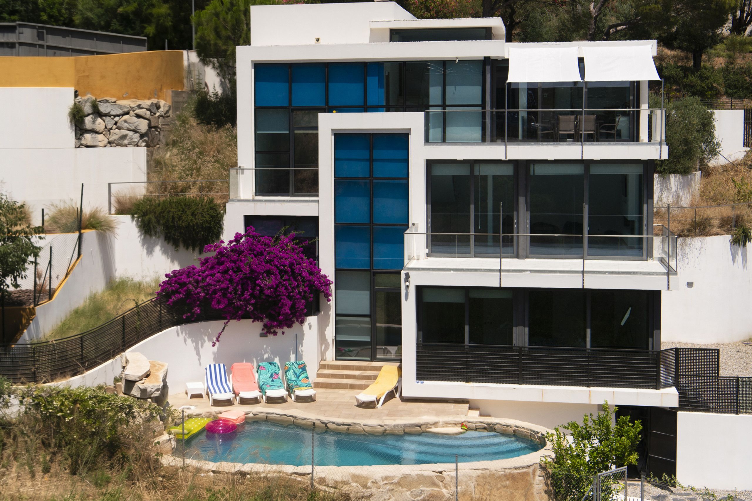 Una casa moderna de dos pisos con piscina, mobiliario exterior y un amplio ventanal.