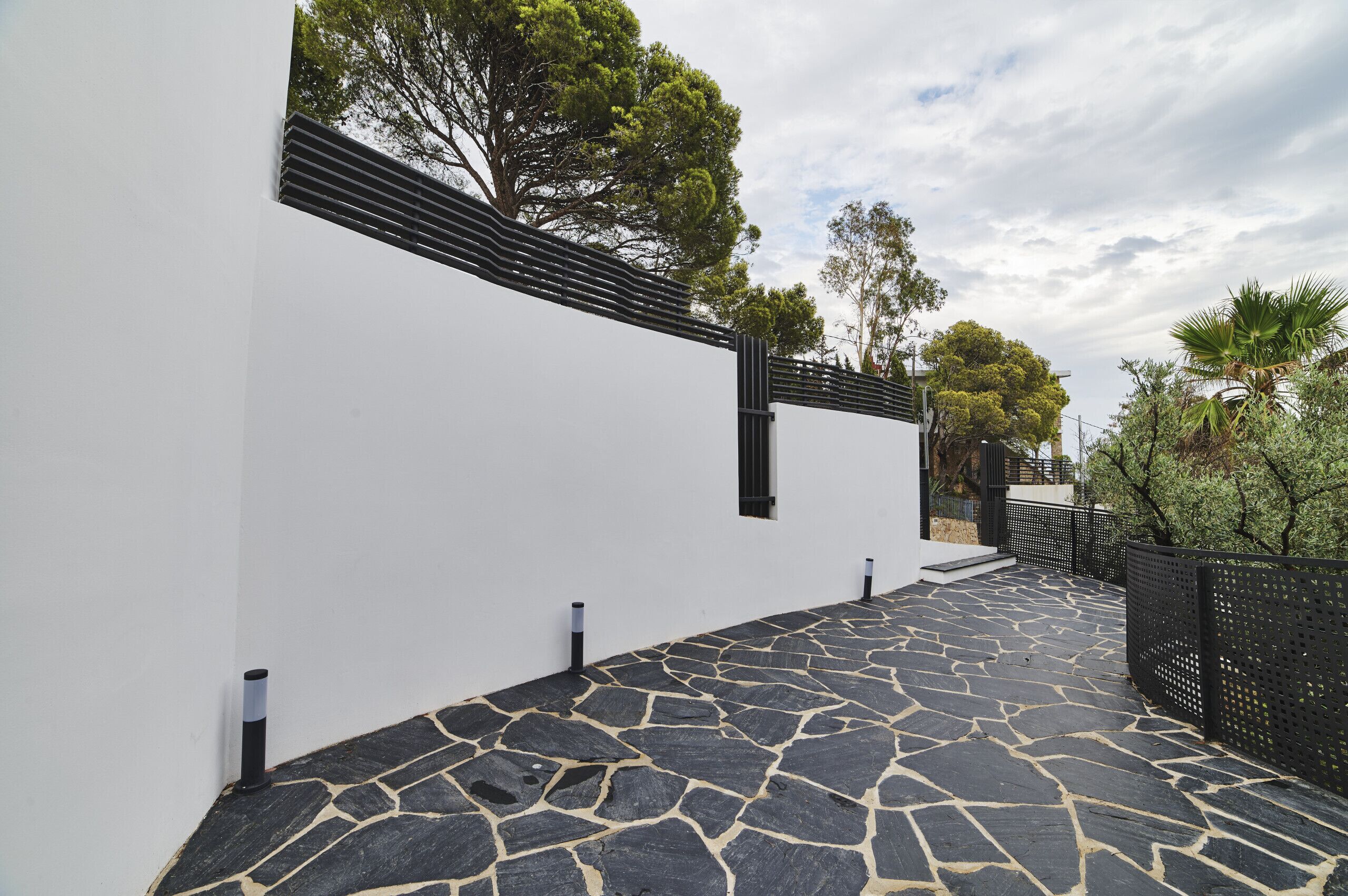 A modern building with a white exterior, a stone-paved pathway, and a black metal fence.