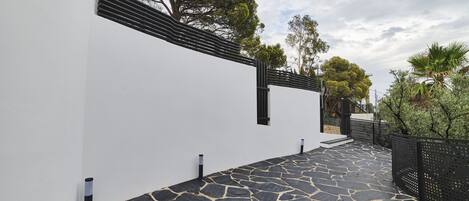 A modern building with a white exterior, a stone-paved pathway, and a black metal fence.
