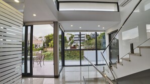 A modern interior with a glass staircase, a patio with outdoor furniture, and a view of surrounding buildings. - WELCS VILLA MODERNA 097 EMP con piscina (Llança)