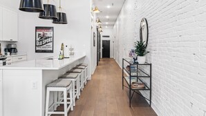 Una cocina moderna con armarios blancos, una isla central con taburetes de bar, iluminación colgante y una pared de ladrillo decorativa.