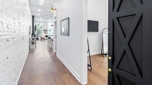 Un interior moderno con pared de ladrillo blanco, suelo de madera y una puerta negra con diseños geométricos.