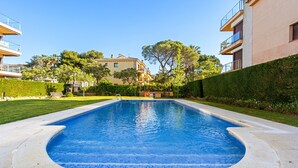 Une piscine dont le bord est recouvert de carrelage, entourée d’une pelouse bien entretenue et d’une haie.