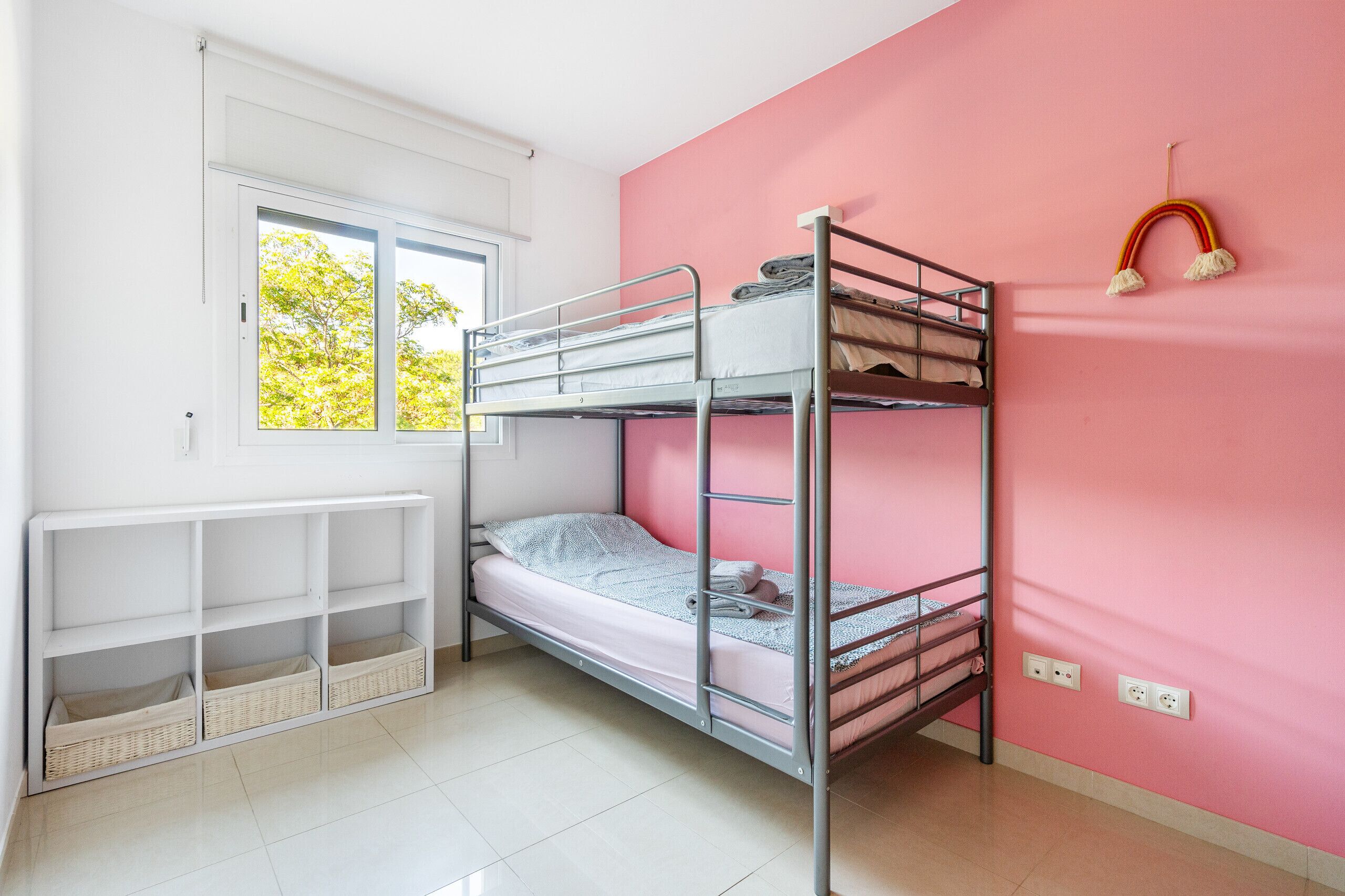 A bunk bed room with a window, white shelves, and a pink wall.