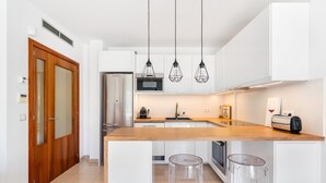Une cuisine moderne avec des meubles blancs, un plan de travail en bois et trois tabourets de bar.