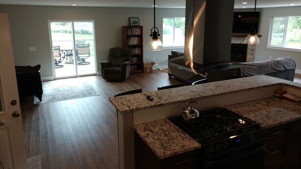 A modern kitchen with a granite countertop, a gas stove, and a large island. There is a dining area with a table and chairs, and a bookshelf filled with books. The room has a large window and a ceiling fan. - Mountain Hideaway Retreat- Room for Everyone (Townsend)