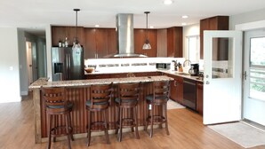 A modern kitchen with a central island, bar stools, stainless steel appliances, and wooden cabinetry. - Mountain Hideaway Retreat- Room for Everyone (Townsend)