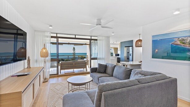 A modern living room with a grey sofa, a round coffee table, and a view of the sea through large windows. - BANNOW7 (Alexandra Headland)
