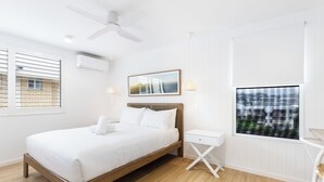 A modern bedroom with a wooden bed, a white nightstand, a ceiling fan, and a window with blinds. - BANNOW7 (Alexandra Headland)