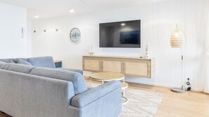 A modern living room with a grey sofa, a round wooden coffee table, a television mounted on a white wall, and a floor lamp. - BANNOW7 (Alexandra Headland)