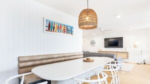 A modern dining area with a white table, wicker chairs, a bench, and a hanging light fixture. - BANNOW7 (Alexandra Headland)