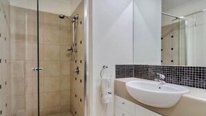 Une salle de bain moderne avec une douche à parois de verre, un lavabo blanc et un mur recouvert de carreaux.