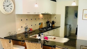 Une cuisine moderne avec un îlot central, des tabourets de bar, une horloge et un lave-linge en arrière-plan.