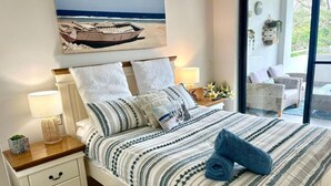 Un lit bien fait, avec une literie à rayures, une table de chevet avec une lampe, et une vue sur l’extérieur grâce à une porte vitrée.