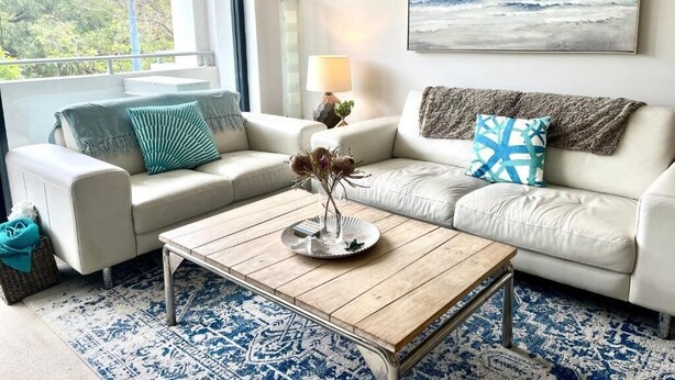 Un salon moderne avec un canapé beige, une table basse et une vue sur l’océan.