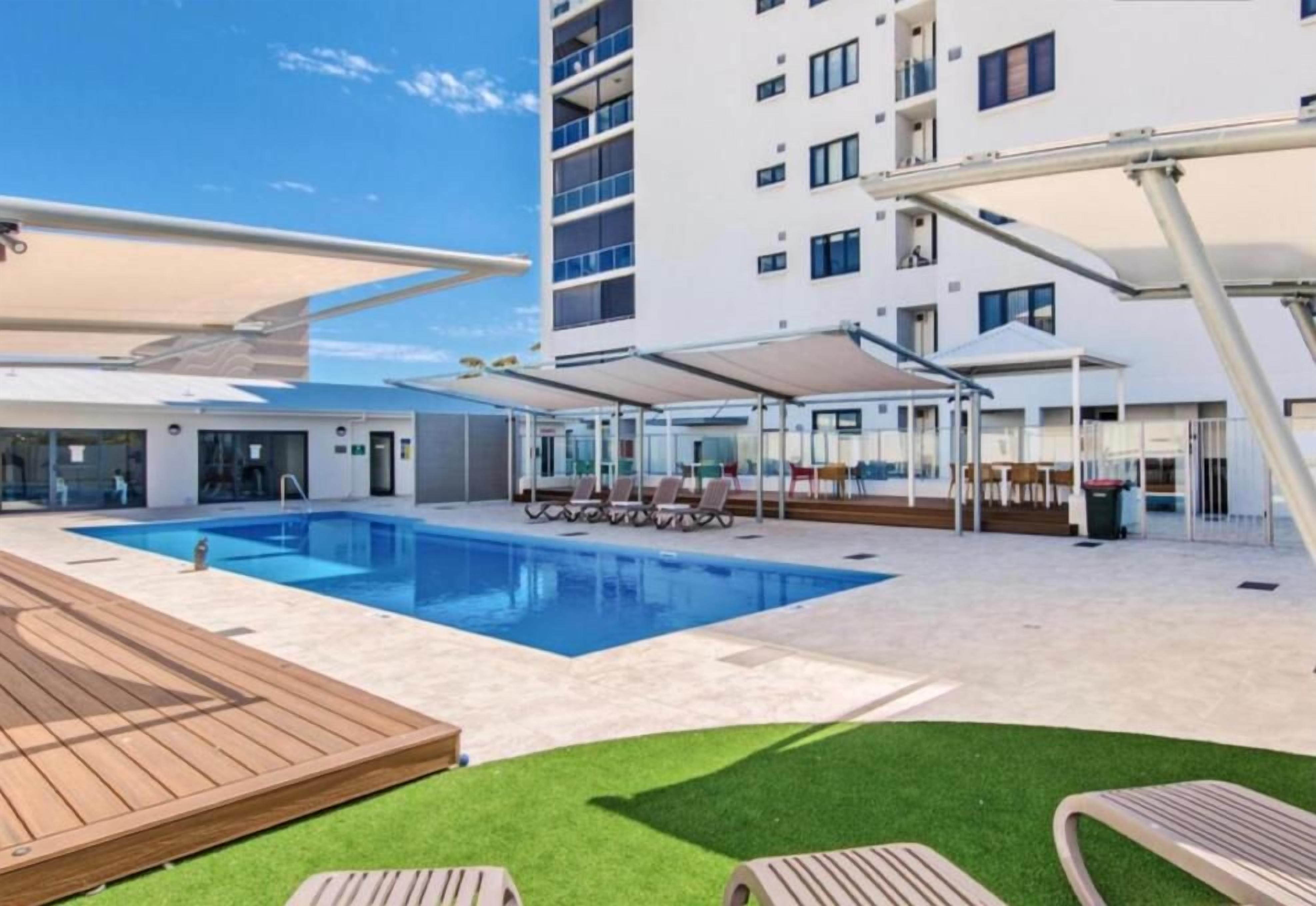 A modern hotel pool area with a clear blue pool, wooden deck, and lounge chairs.