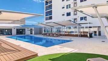 A modern hotel pool area with a clear blue pool, wooden deck, and lounge chairs.