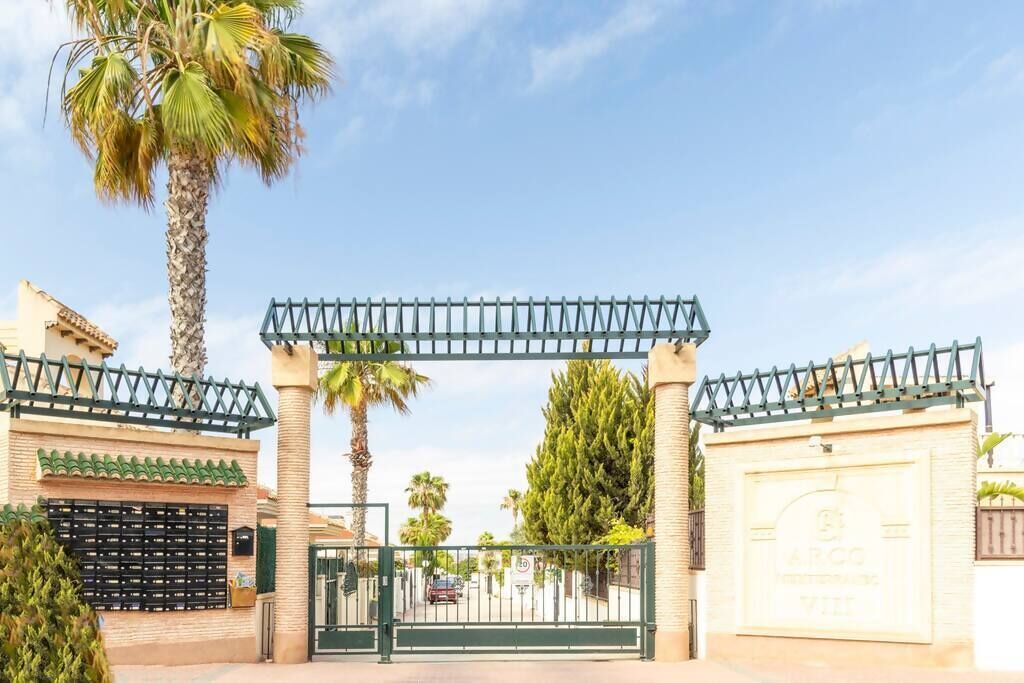 A gated entrance with a palm tree and a building with a tiled roof.