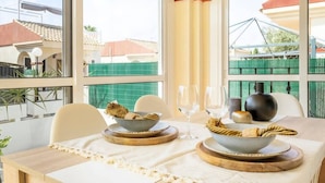 Een eetgedeelte met een tafel gedekt voor twee personen, met een witte tafelkleed, twee kommen met gevlochten placemats en een wijnglas.