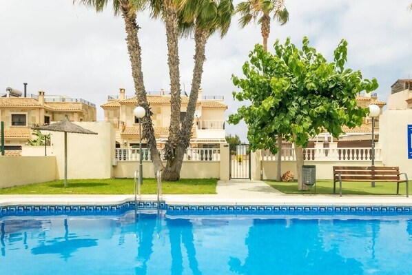 A swimming pool with a tiled edge, surrounded by palm trees and a bench.